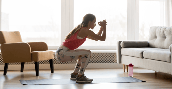 Sporty young woman doing squat morning exercise alone in living room